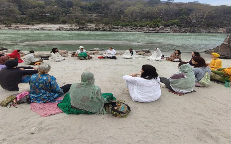 A group sitting together by the Ganga with the mountains behind
